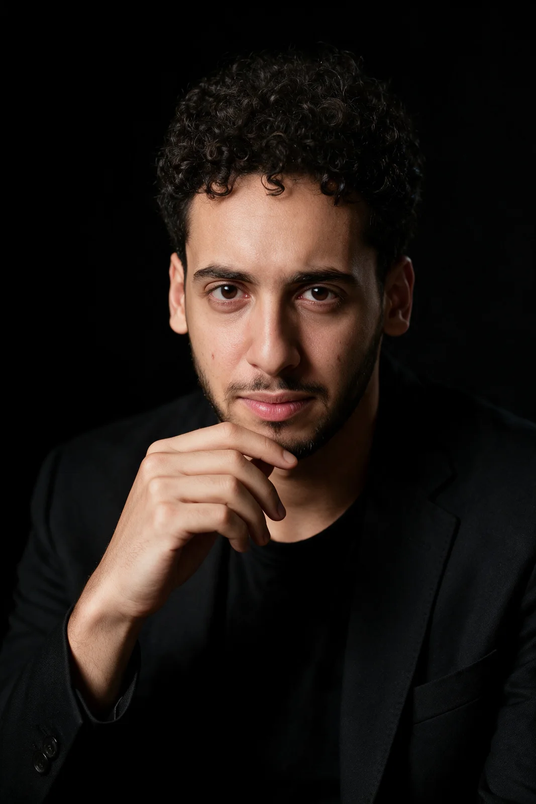 Editorial portrait of Zein Kaskas in a thoughtful hand-to-chin pose under high-contrast low-key lighting against a black background.